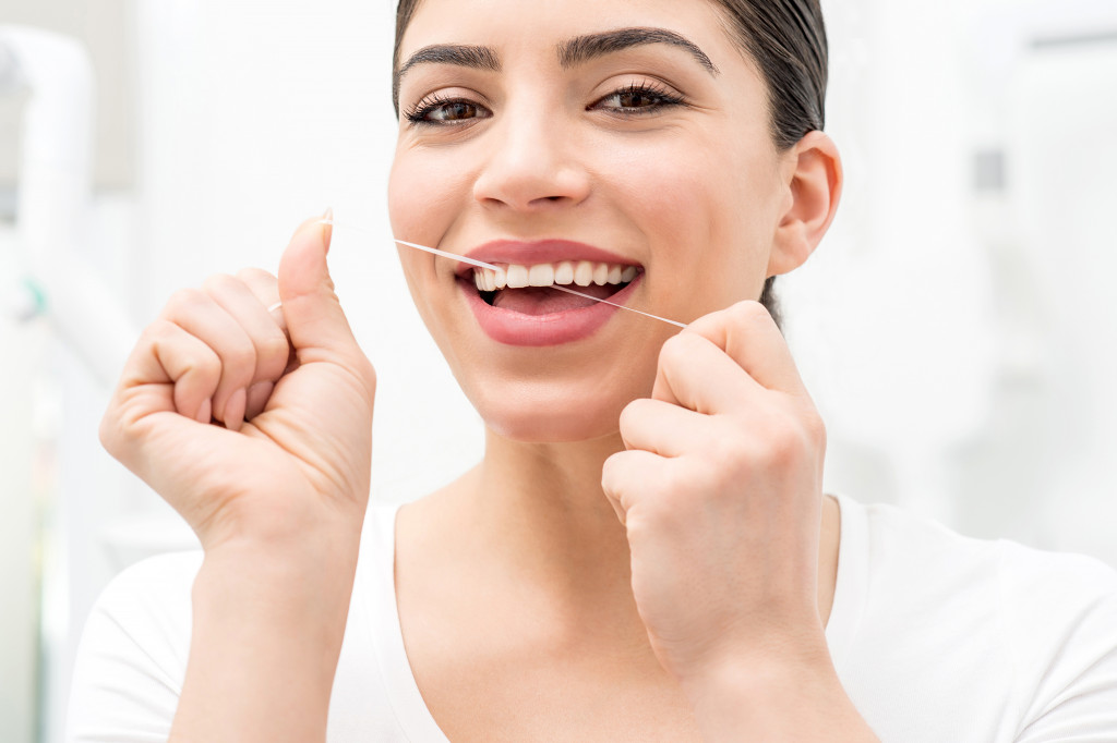 Woman using dental floss for cleaning her teeth