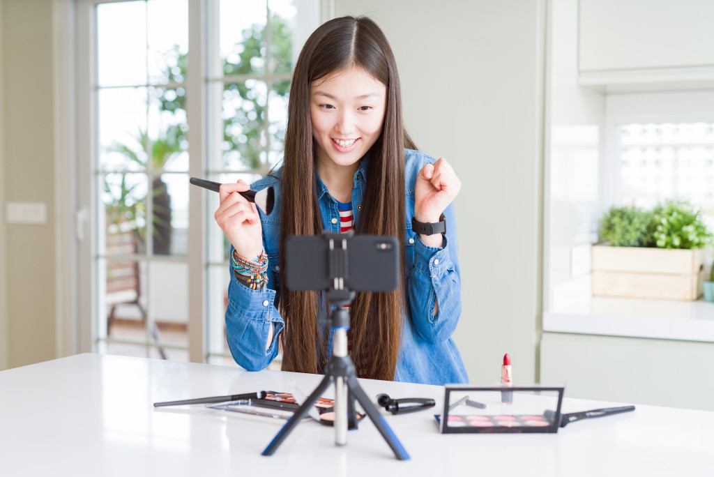 A woman recording in front of a phone on a tripod, make up products for a make up video