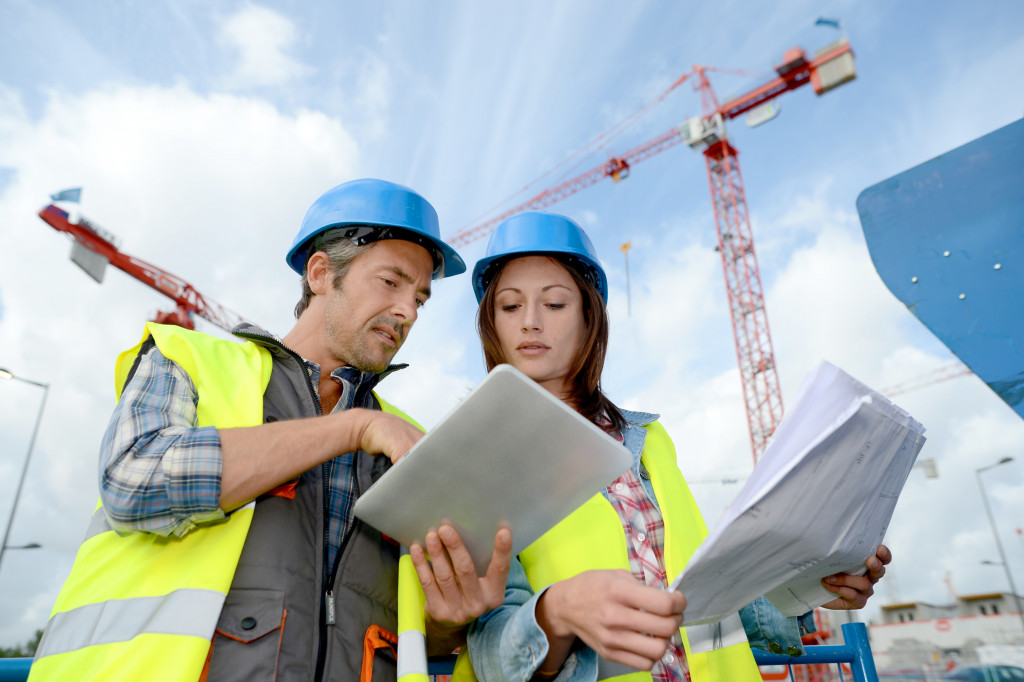 two people holding blueprints and talking in a construction site