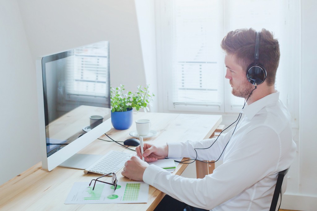 A businessman watching a tutorial on his home office desktop while taking notes