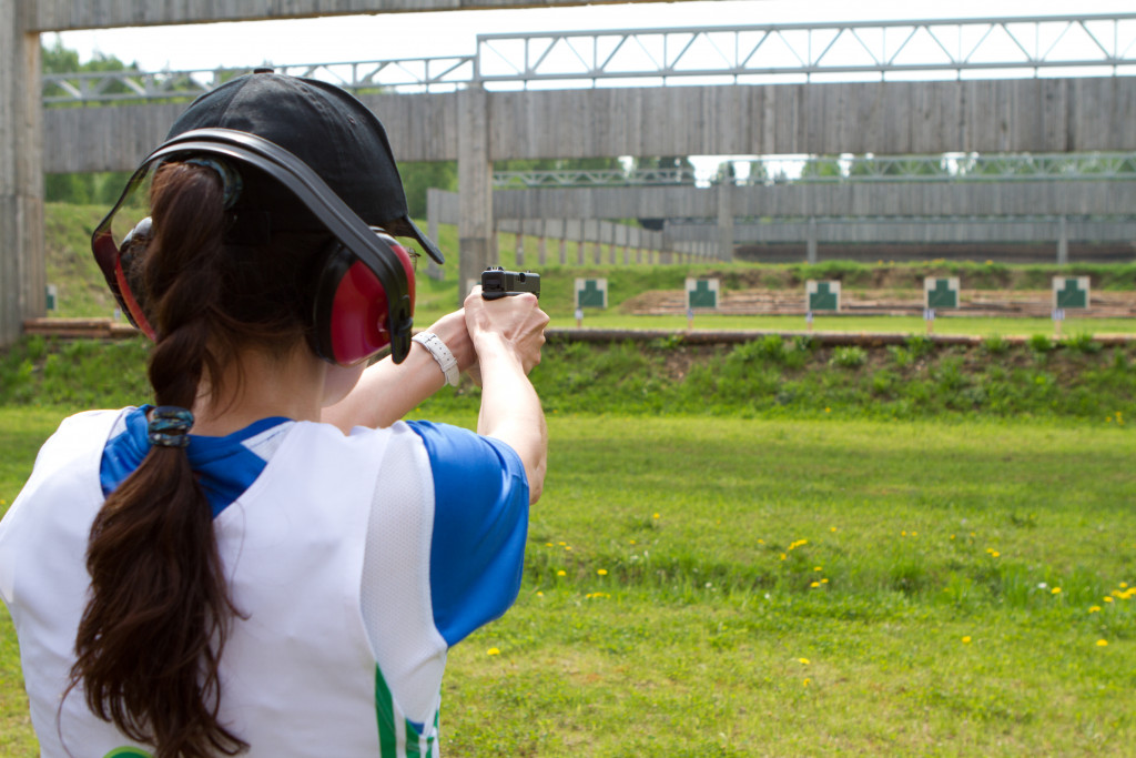 A woman wearing noise-suppression earmuffs holds a Glock and aims down the shooting range at paper targets