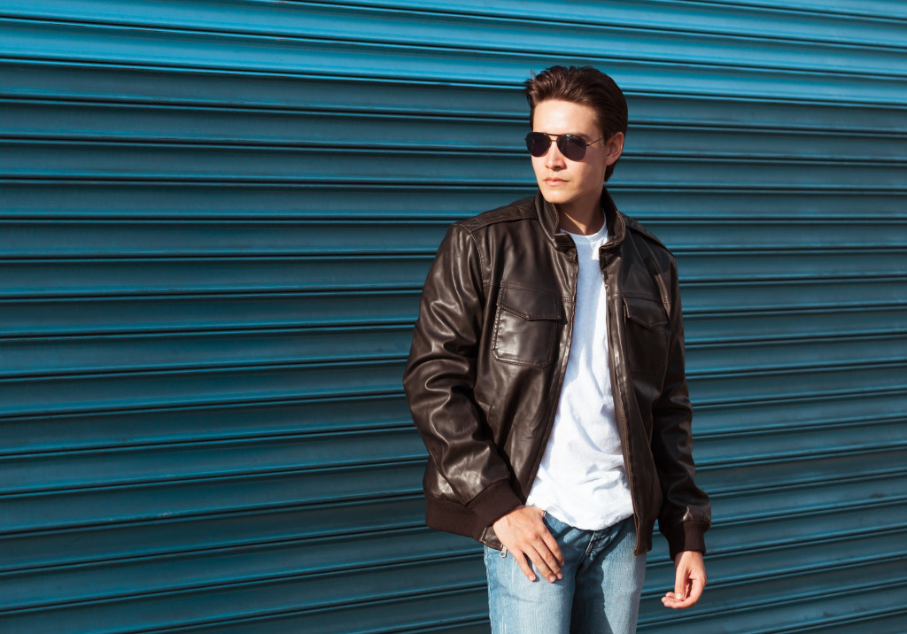 a male model with sunglasses wearing a brown leather jacket