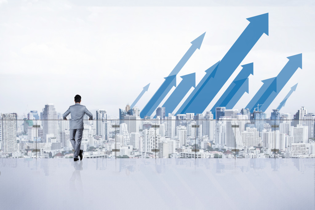  Business executive standing at a balcony looking at a city skyline and arrows pointing upwards.