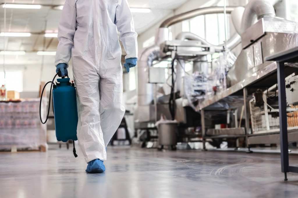 person in protective suit carrying a disinfectant machine along a factory corridor