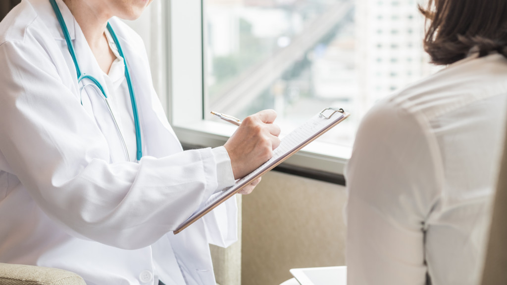 female doctor taking down notes while interviewing female employee patient