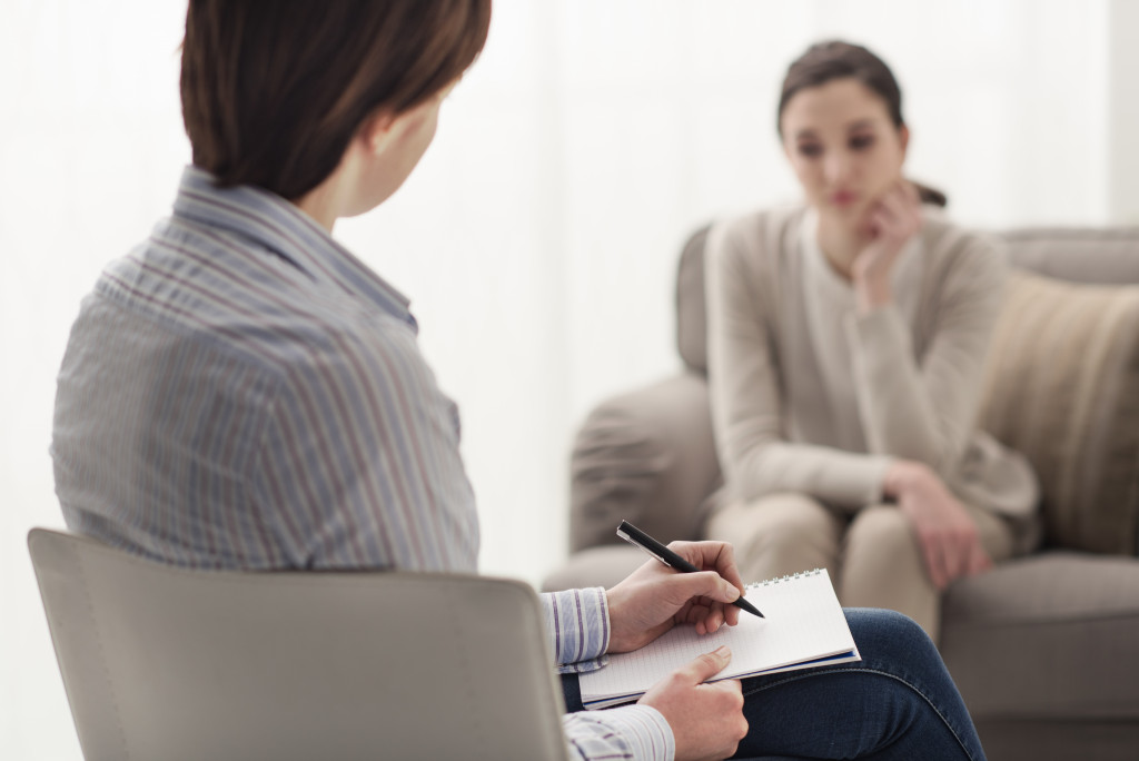 female therapist taking down notes while talking to female patient sad on the couch