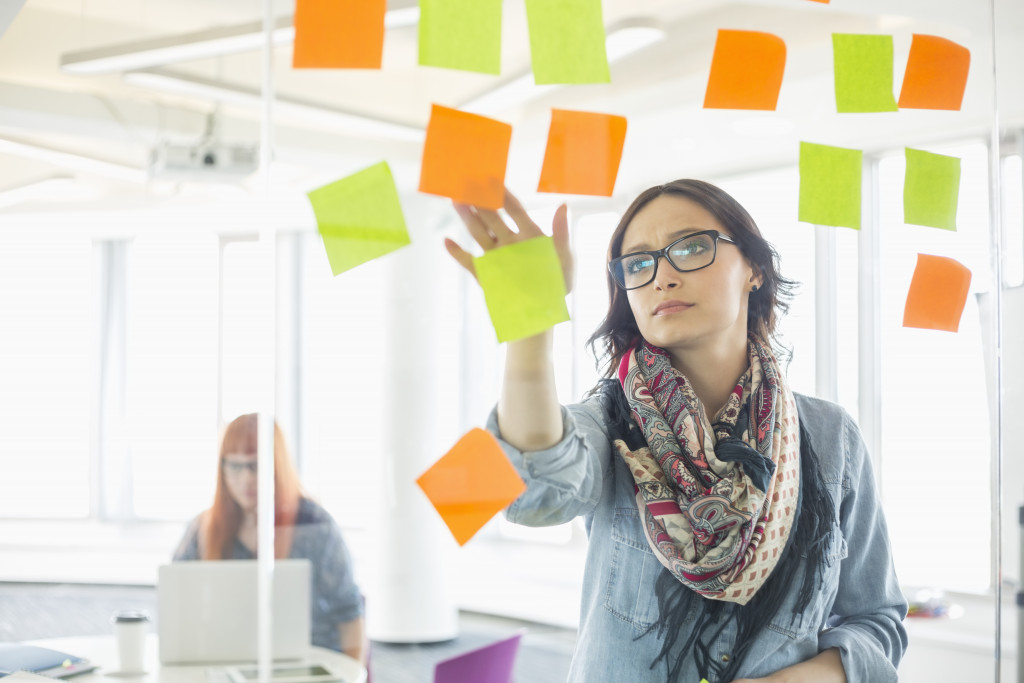 woman with glasses pasting post-it notes of yellow and orange in glass to plan her schedule