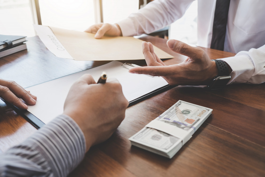 male applicant signing document in clipboard for a loan with money on the side