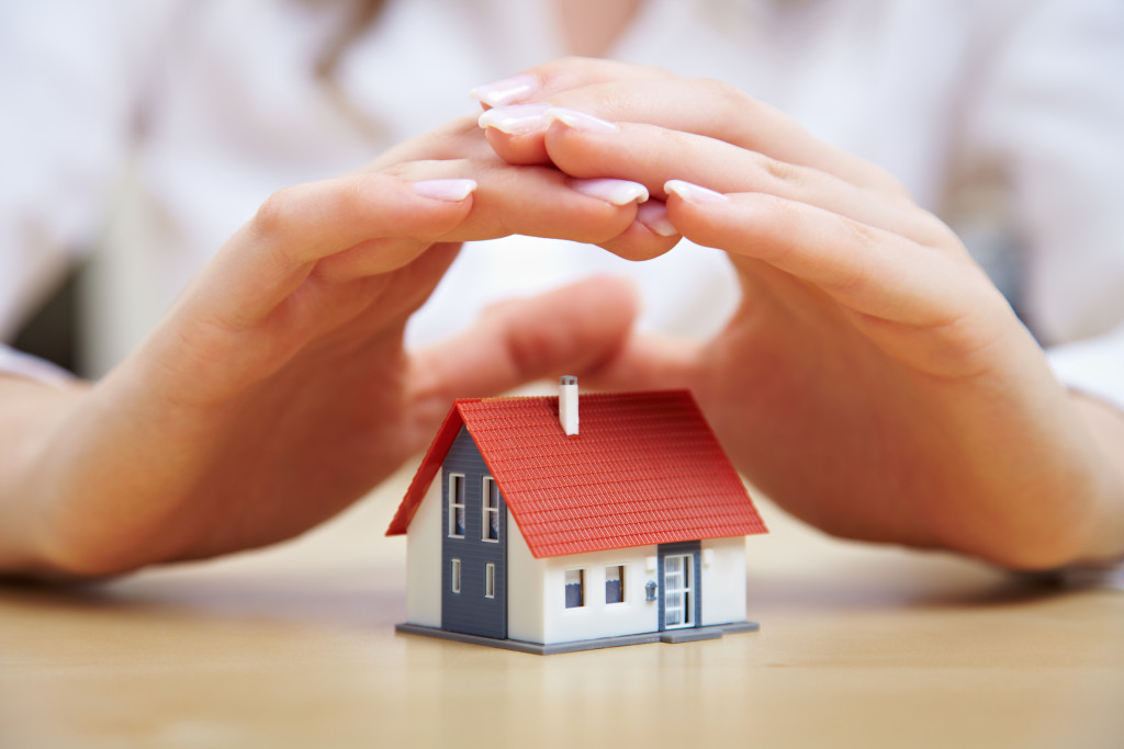 woman's hands protecting a miniature house model in a wooden table