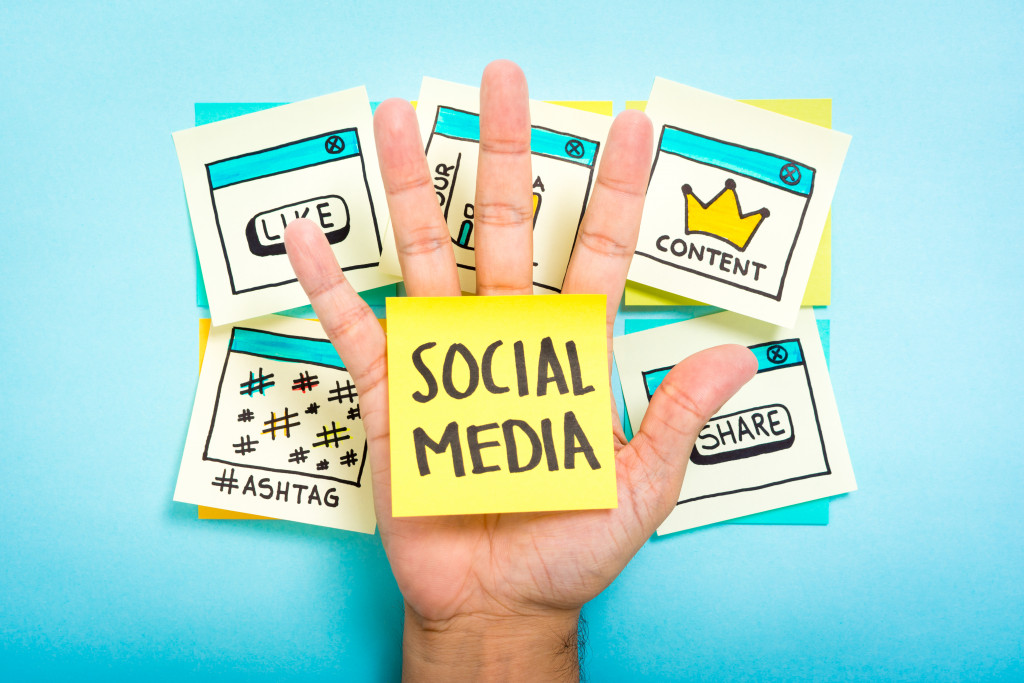 hand with yellow sticky note with words social media and other icons at the back